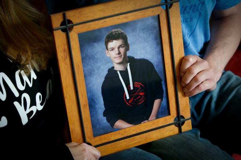 Two people hold a framed photo of a teenaged boy.