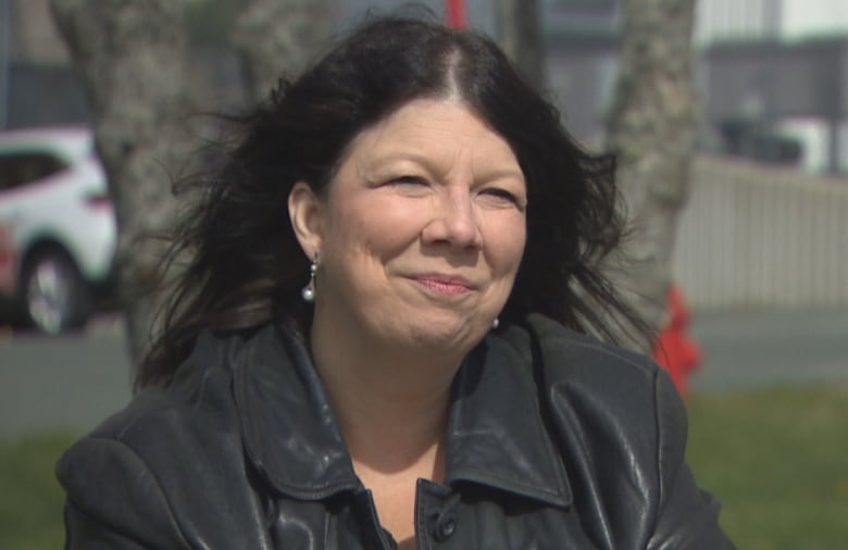 Woman with dark hair being blown back by wind wearing a black jacket.