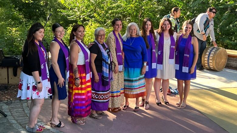 Indigenous graduates of McMaster University stand in a line and pose for a picture alongside Indigenous elders.