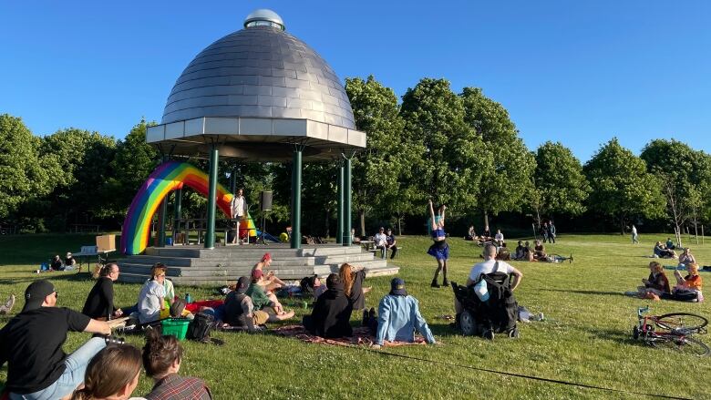 People in a park watch a drag artist perform.