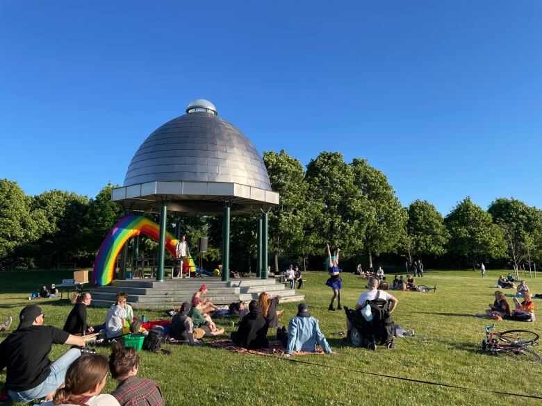 People in a park watch a drag artist perform.