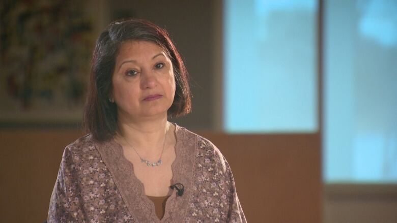 A woman stares at a camera, with a blurred background that shows a window.