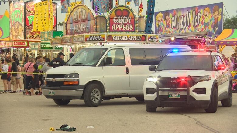 Police vehicles are parked in front of rides and games at a fairground.