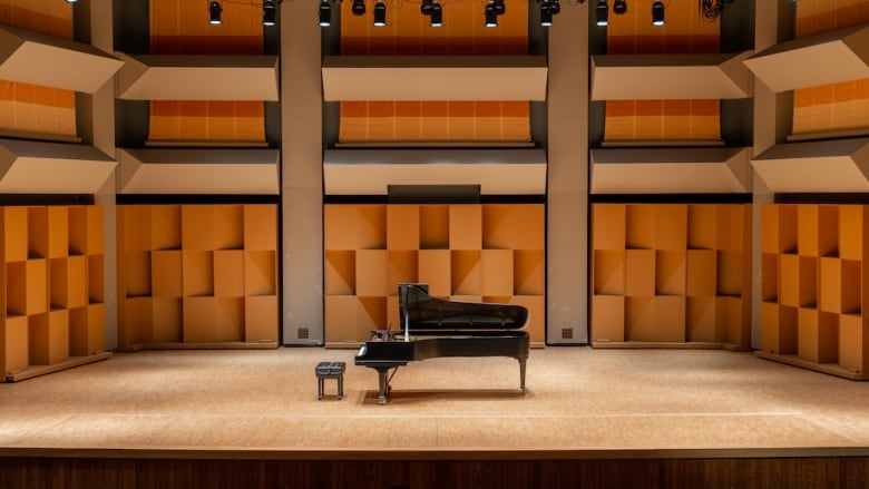 A concert grand piano alone on a large empty stage.