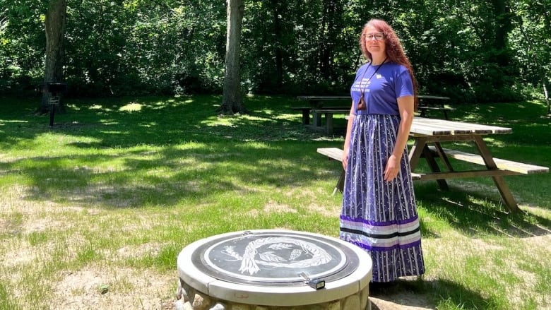 Woman stands near a fire pit.