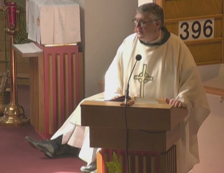 A man dressed in priest's robes speaks at a lectern in a Roman Catholic church. 