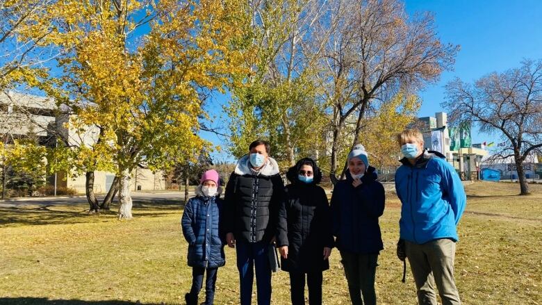 Five people in jackets and masks pose for a photo on a sunny, fall day. 