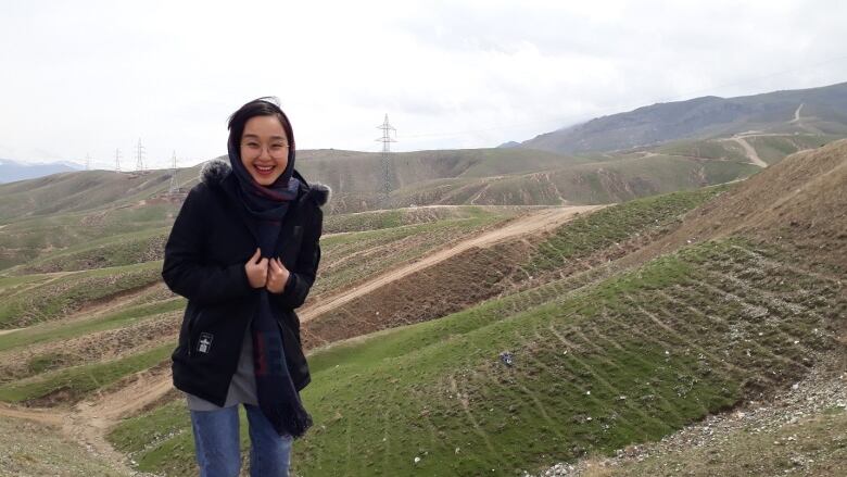 A woman smiles with Afghanistan's mountains behind her.