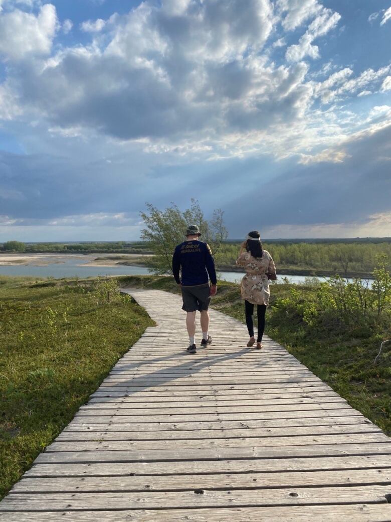 A man and a woman walk on a boardwalk on a sunny day.