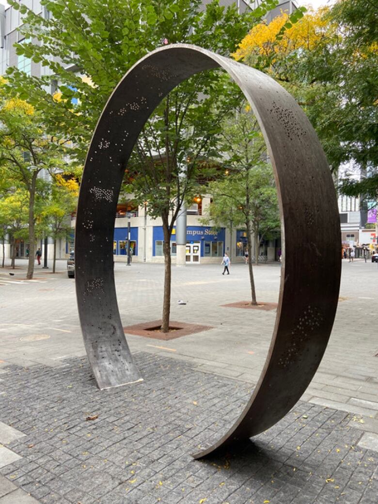 A large monument the shape of a ring stands on the campus of Toronto Metropolitan University. It is as tall as a small tree and features tiny perforations representing animal symbols.