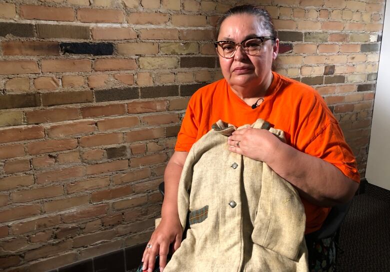 Woman in an orange shirt holds a child-sized beige jacket.