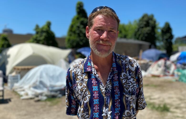 A man pictured in front of several tents set up on a plot of land.