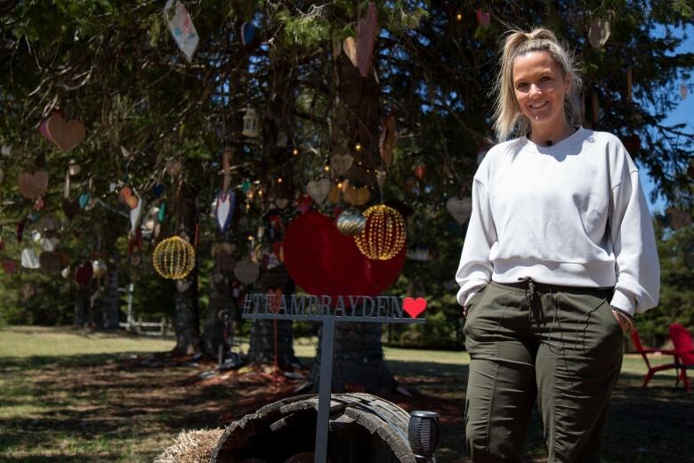 Woman stands in front of tree decorated with tributes to boy and his family.