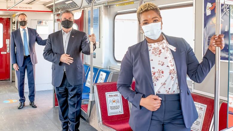 Three people wearing masks stand in a subway train.