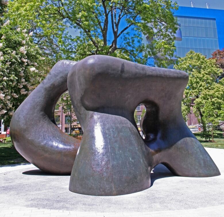 Daytime photo of Large Two Forms, a monumental bronze sculpture of the late Modern period. It resembles two enormous pelvic bones. The work is installed in a green park.