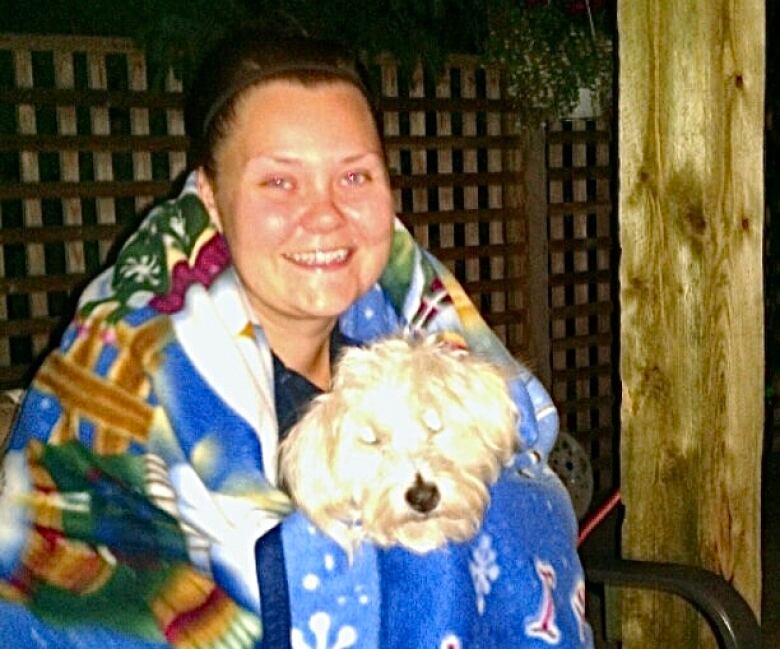 A woman sits with a blanket wrapped around her, holding a dog.