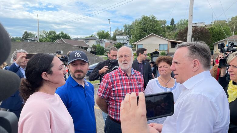 Woman in a parking lot talking to the premier, as a small group listens.