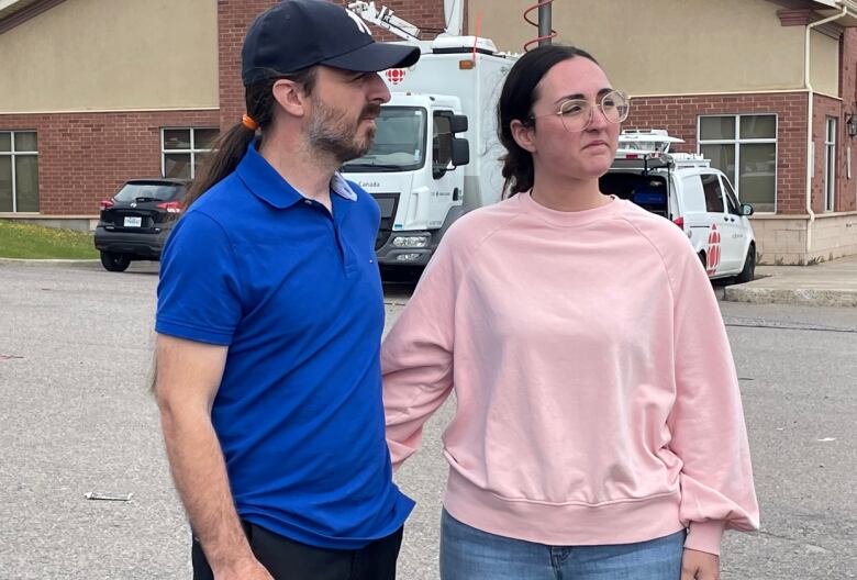 A couple stands in a parking lot.