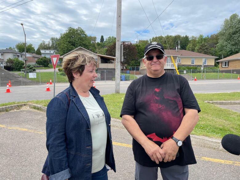 An older couple stand in a parking lot.