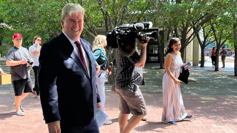 A smiling man in a suit looks toward the camera, as photographers walk alongside him.