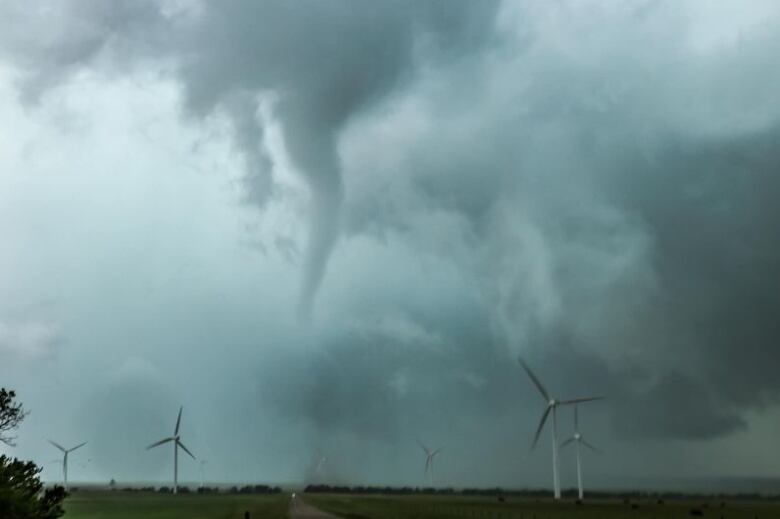 A funnel cloud dips from the clouds near Rheinfeld, Saskatchewan, where a wind farm is located. Several wind turbines are visible. 