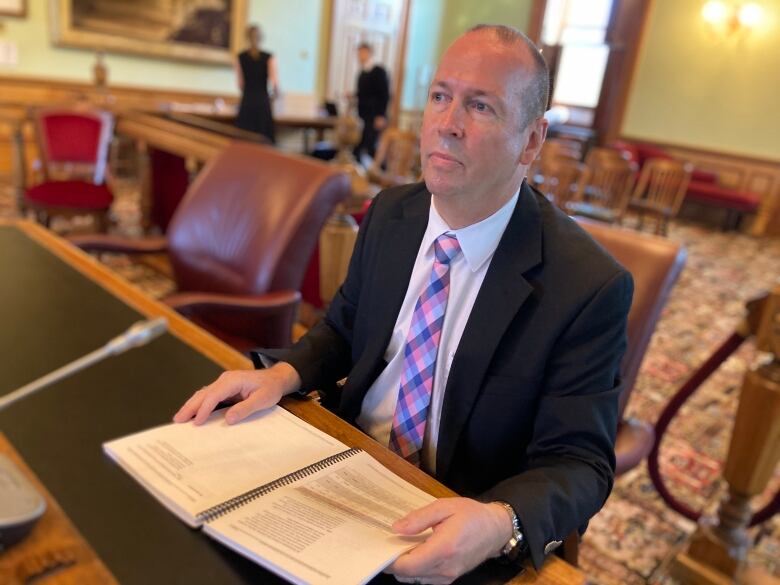 A man in a suit sitting at a desk and holding an open book