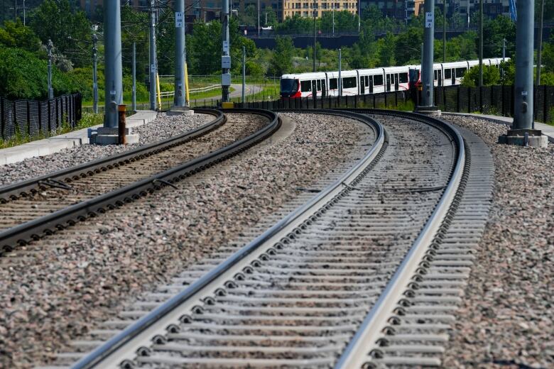 A red and white light rail train on the tracks in the distance.