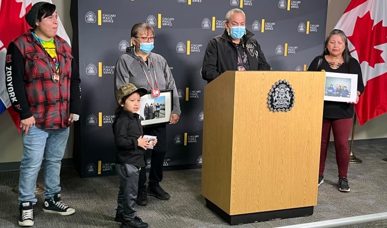 Five members of a family gather around a police podium holding photos of their loved one. 