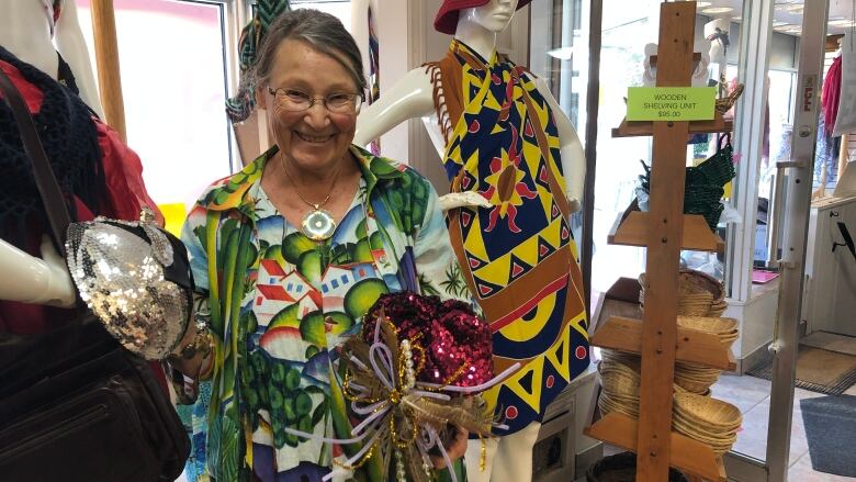 A woman in a colourful dress holds two hats inside a clothing store.