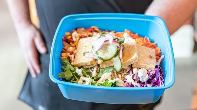 Server holds blue reusable takeout container with a salad inside.