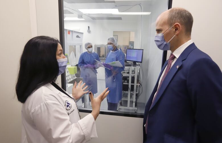 A woman in a lab coat talks to a politician in front of a laboratory.