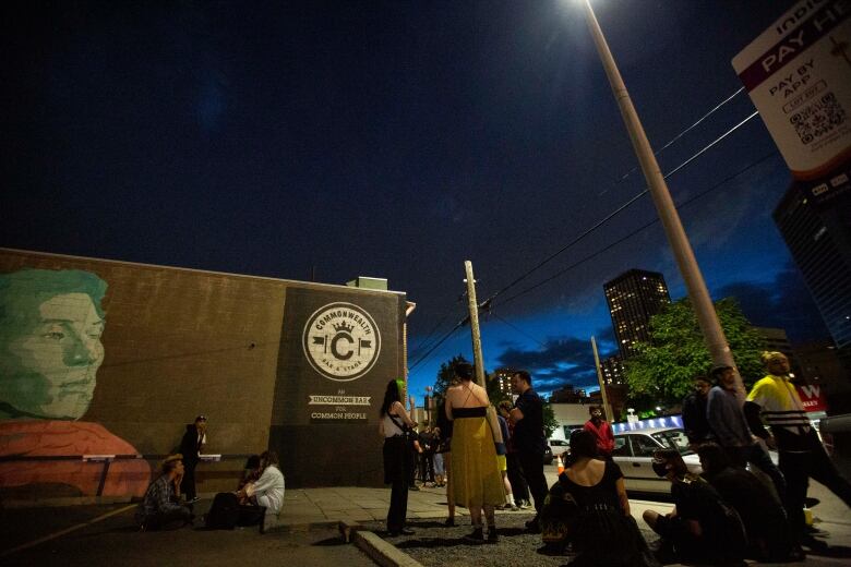 people stand in a parking lot underneath a dark evening sky 