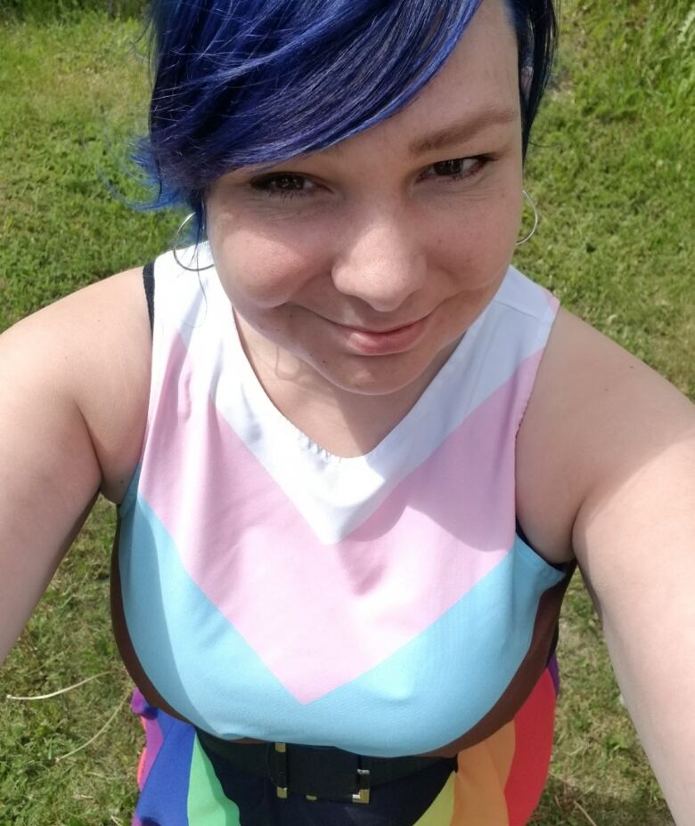 Someone takes a selfie from above. They are wearing a dress made in the colours of the Pride flag, and they are standing outside.