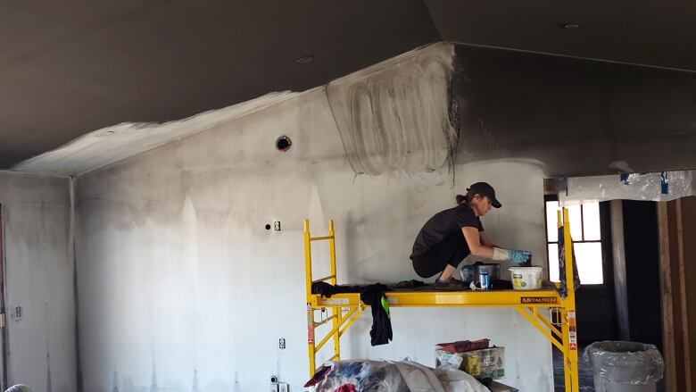 A worker standing on scaffolding scrubbing soot off the wall in the Salsman home.