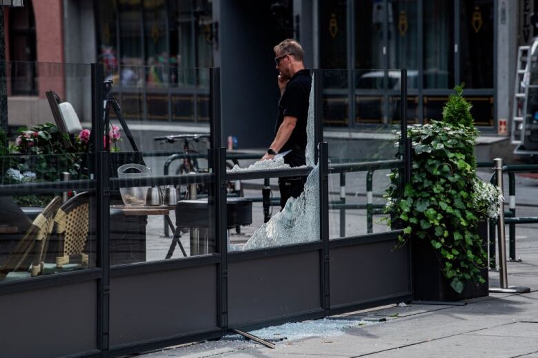 A man who appears to be on the phone stands near shattered glass.