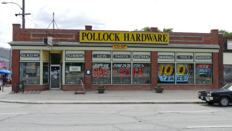 A brick building is pictured with part of a black car in the foreground.