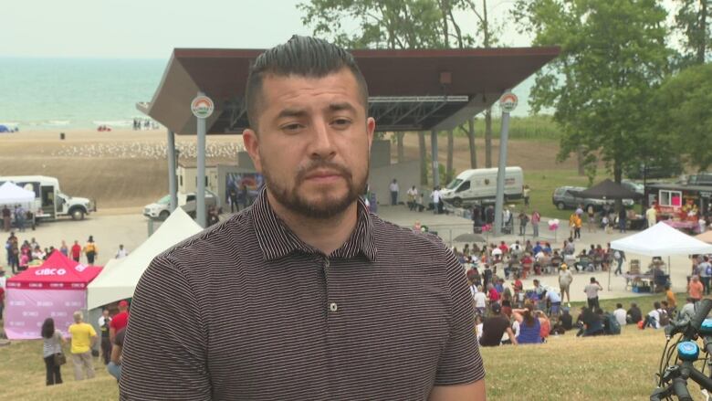 A man looks serious, standing with a festival behind him. 