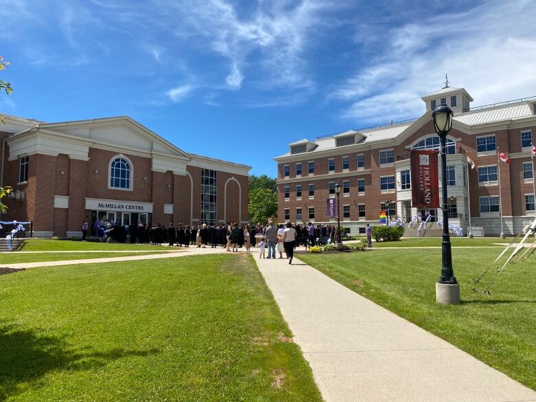 Sunny day on grassy college campus with graduates in gowns entering a brick building that says MacMillan Centre.