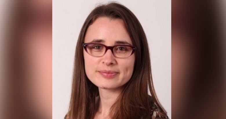 A woman with glasses and shoulder-lengh brown hair poses for a portrait.