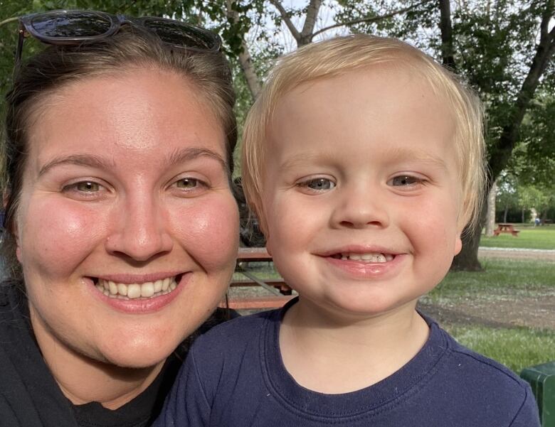 Woman and young boy smile outdoors.