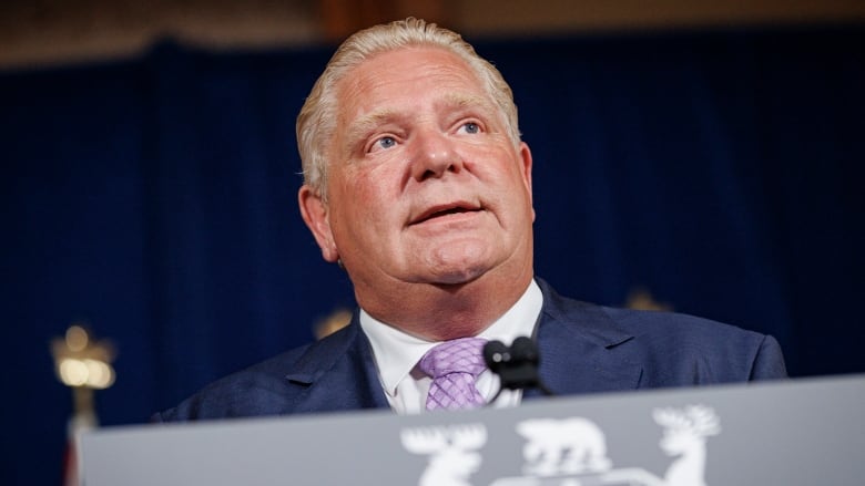 A man in a suit speaks at a lectern.