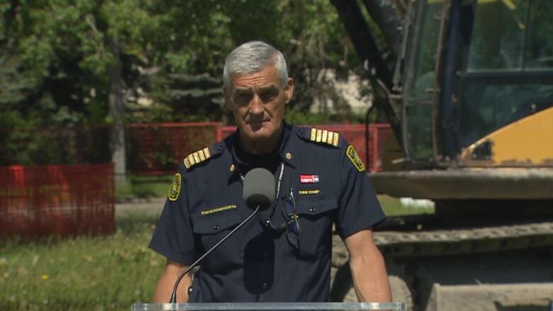 A man wearing a blue and gold uniform stands in front of a yellow crane. 