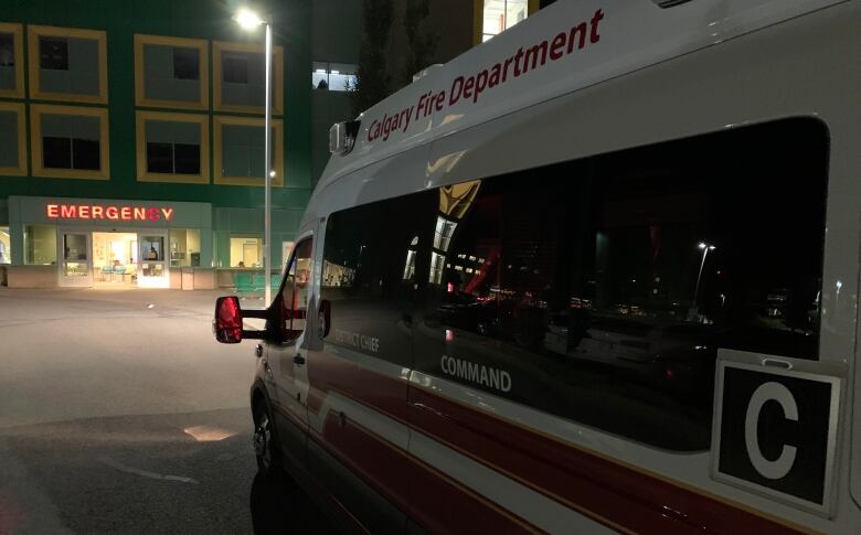 A red and white van in front of a green building and a red sign which reads emergency. 