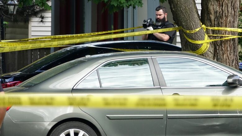 A police officer surrounded by crime tape uses a camera.