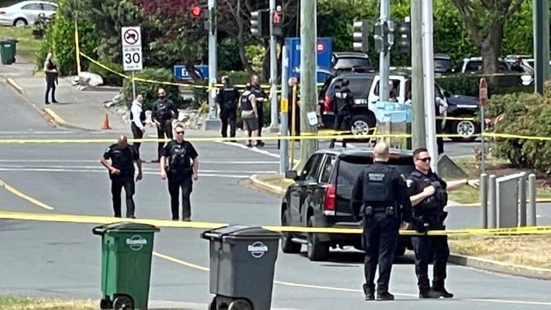 Officers stand behind yellow tape on a street. 