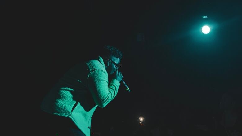 A man sings into a microphone in front of a dark stage.