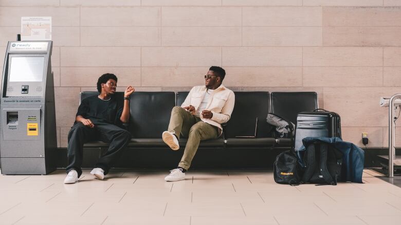 Two Black men sit on an airport couch.