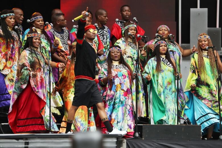 A photo of a Black man performing in front of a choir of women.