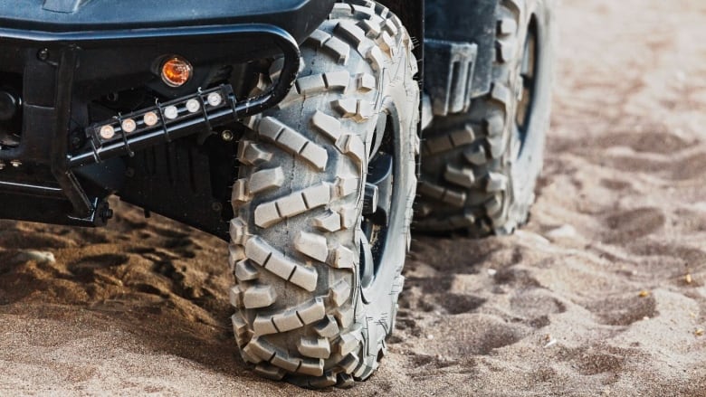 A closeup shows the tires of an all-terrain vehicle on sandy ground.