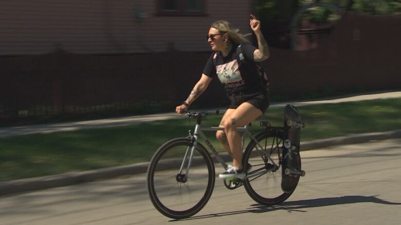 A woman on a bike gives a hand signal as she rides down a city street.